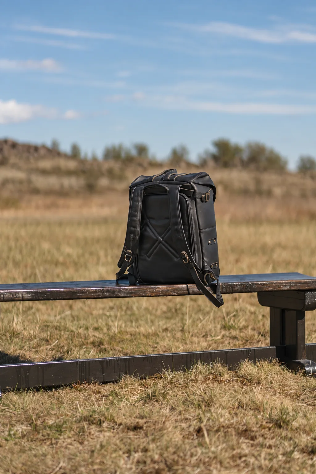 Black leather backpack with both shoulder straps visible resting on an outdoor bench