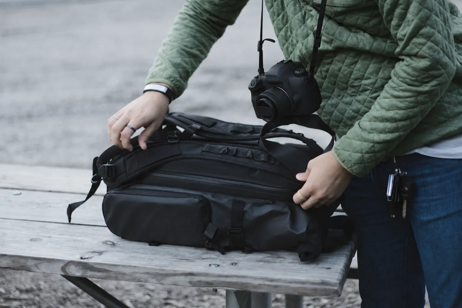 Open black duffel bag on a bench with its pockets visible while a person checks the interior